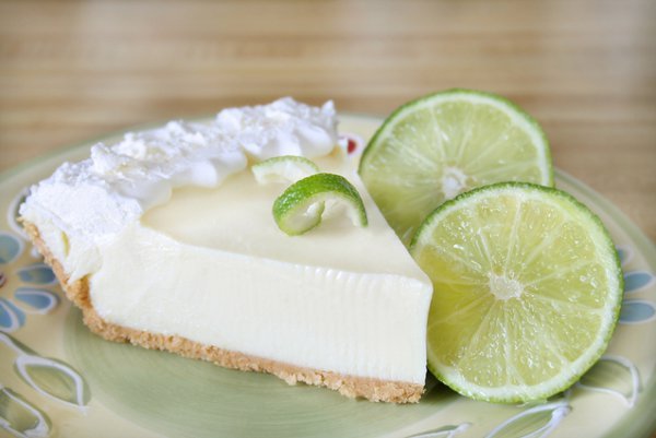 Una porción de pastel de lima con cobertura de crema, acompañada de rodajas de lima, sobre un plato decorativo.