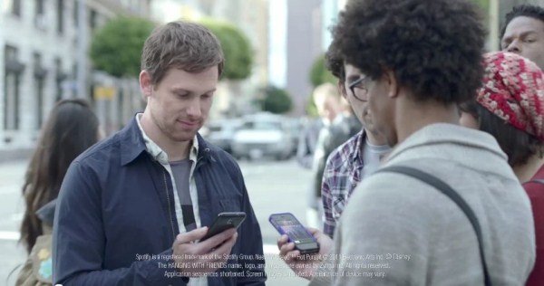 Eine Gruppe von Menschen steht auf der Straße und schaut auf ihre Smartphones. Ein Mann in der Mitte ist besonders fokussiert.