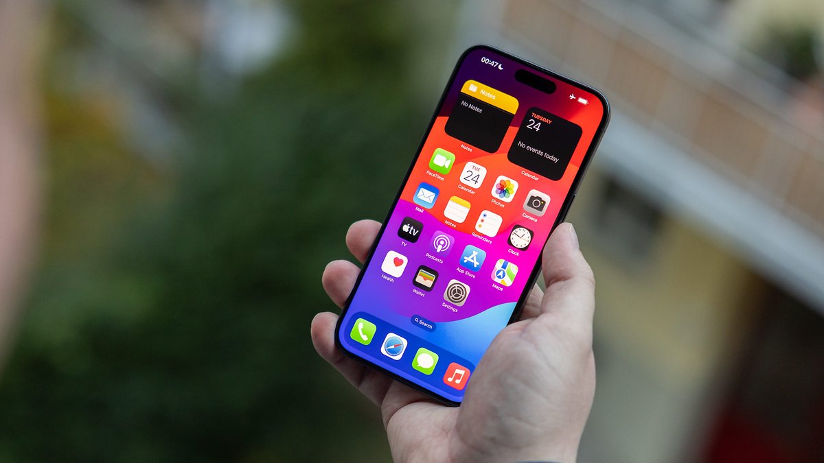 L'iPhone 15 Pro Max vu de face, tenu dans une main droite avec son écran allumé qui affiche l'écran d'accueil d'iOS 17